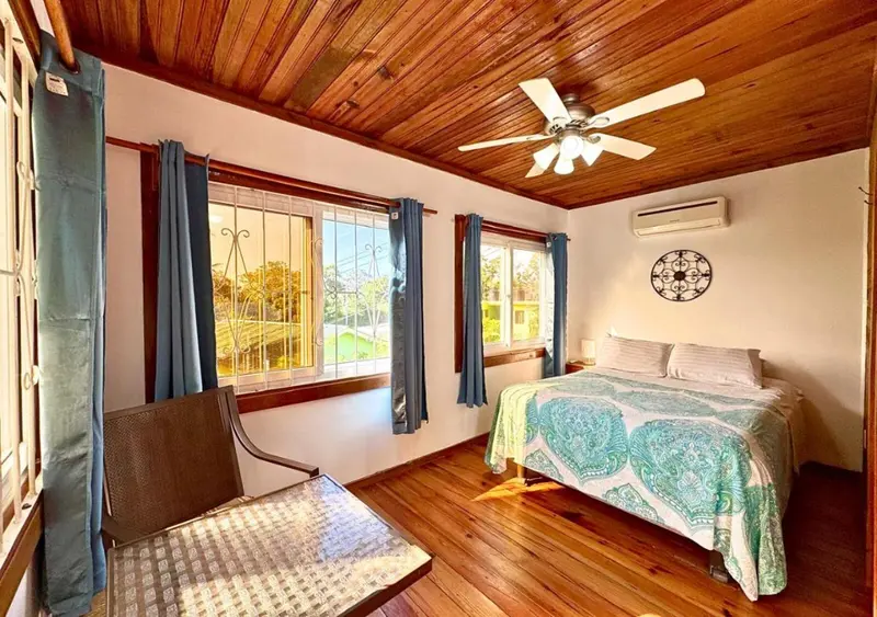 Une chambre lumineuse avec un lit recouvert d'une courtepointe et un ventilateur au plafond.