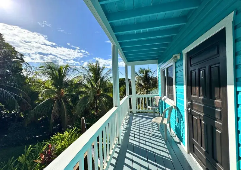 Terrasse en bois bleu turquoise avec une chaise longue et une vue sur la végétation tropicale.