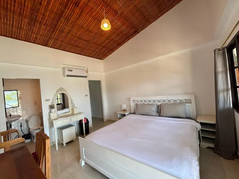Une chambre lumineuse avec un lit blanc et un coin toilette.