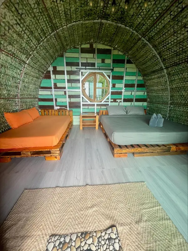 Une chambre aux murs colorés et au sol en bois présente deux lits simples et un tapis.