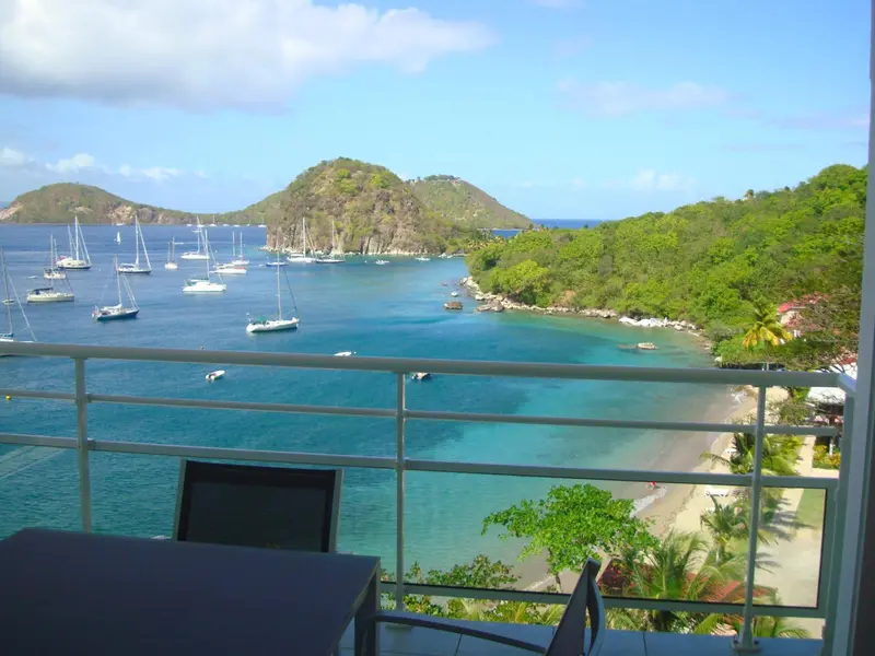 Vue sur une baie turquoise et une côte verdoyante depuis une terrasse.