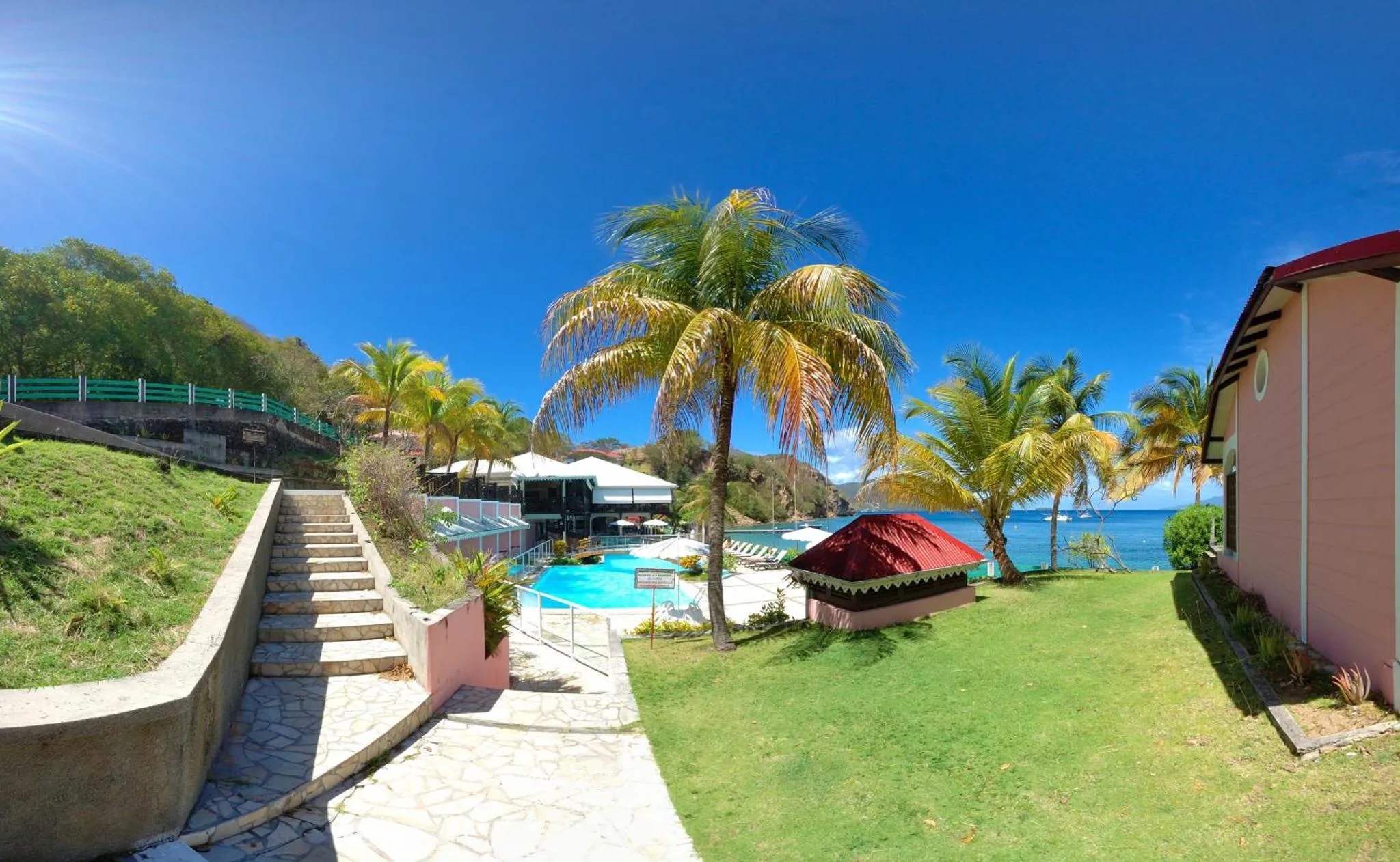 Escaliers descendant vers une piscine au bord de mer, entourée de végétation tropicale.