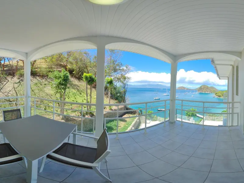 Terrasse carrelée avec mobilier d'extérieur donnant sur une vue mer et des bateaux.