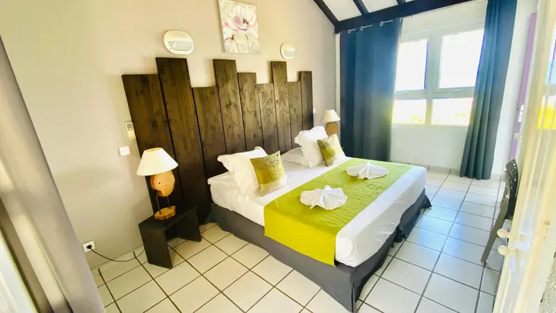 Une chambre lumineuse avec un grand lit recouvert d'une courtepointe verte et jaune.