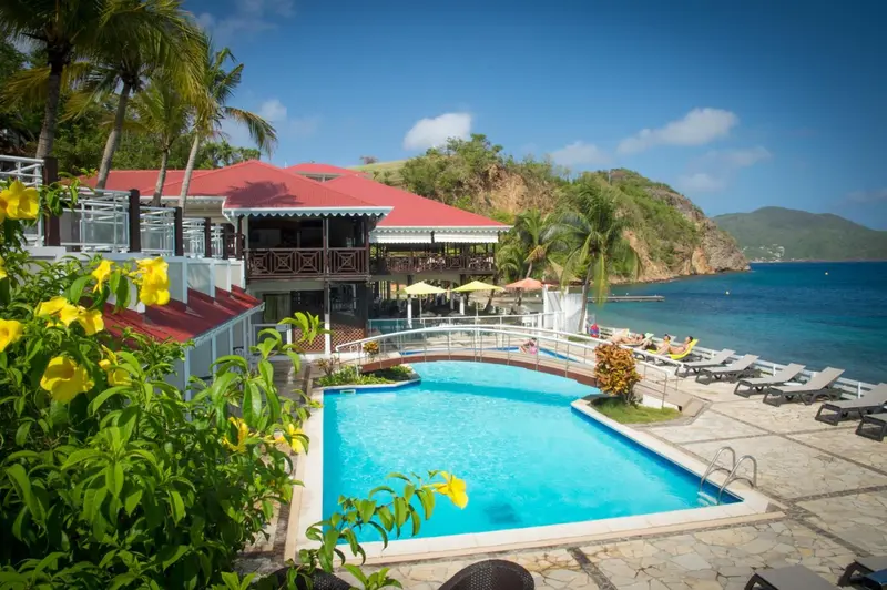 Une piscine turquoise bordée de transats, devant un bâtiment blanc et une végétation luxuriante.
