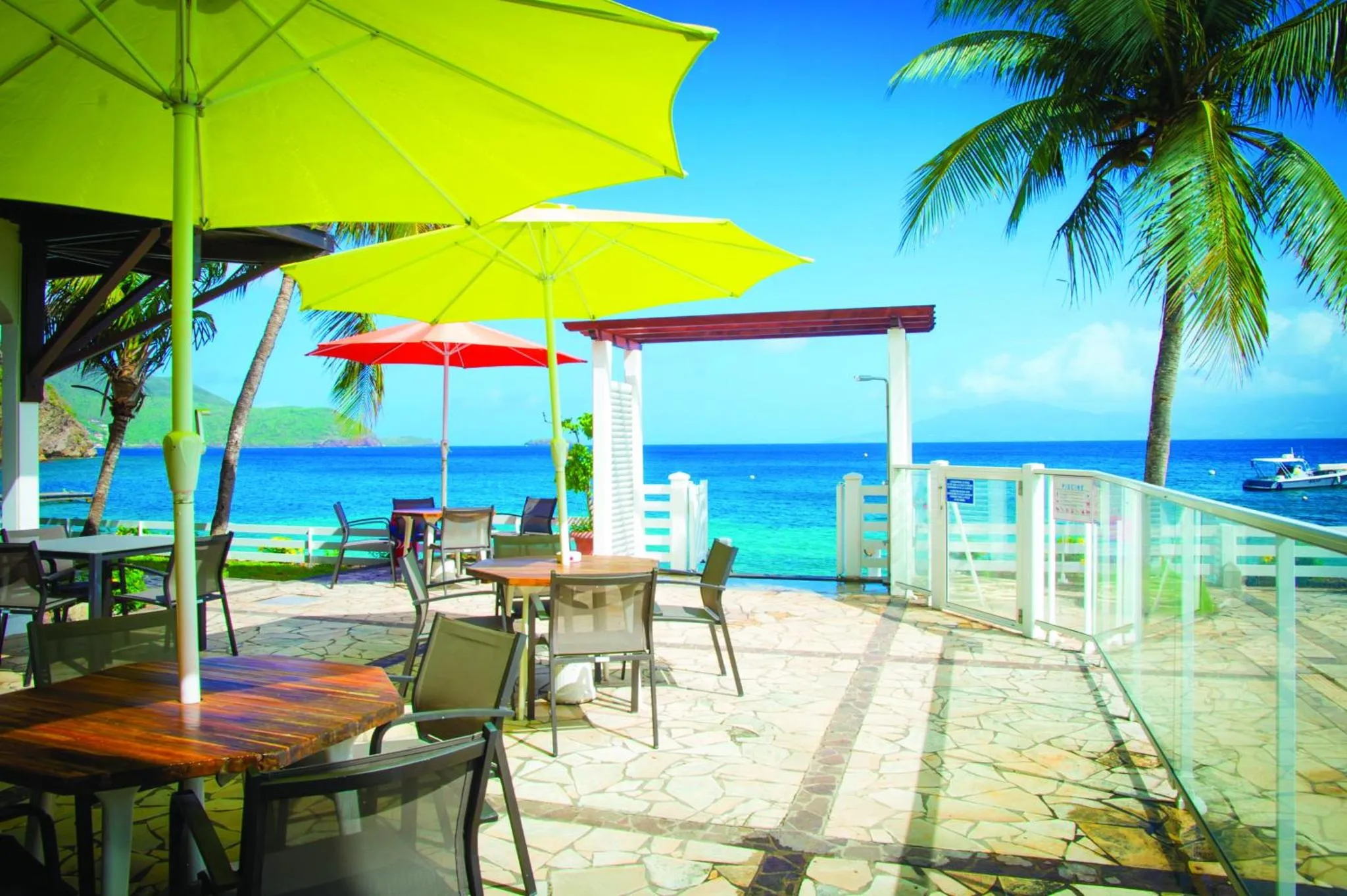 Terrasse ombragée avec tables et chaises donnant sur la mer.
