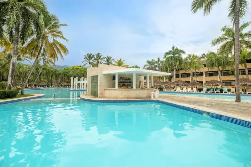 Une piscine turquoise bordée d'une terrasse avec un bar et des palmiers.