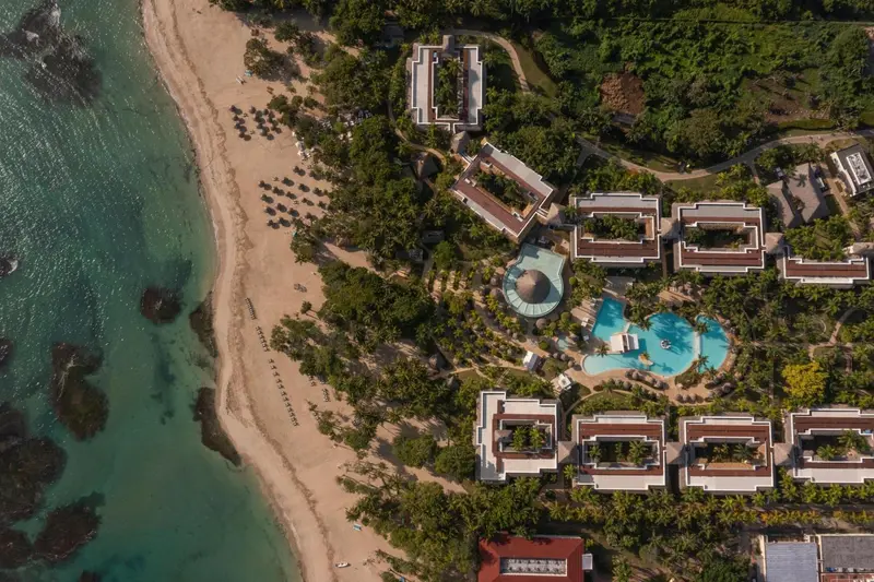 Vue aérienne d'un complexe hôtelier bordant une plage de sable fin et une mer turquoise.