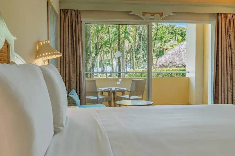 Une chambre lumineuse avec vue sur une terrasse et une végétation tropicale.