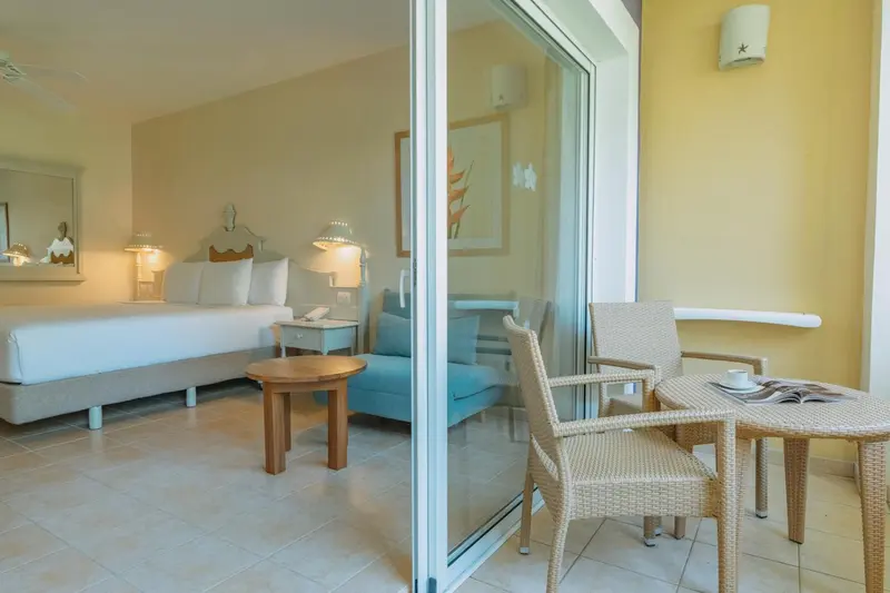 Une chambre lumineuse s'ouvre sur une terrasse avec des fauteuils en osier.