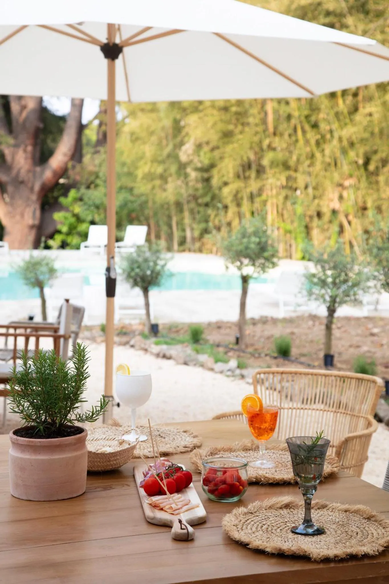 Une table en bois est dressée avec des boissons et des amuse-gueules près d'une piscine.
