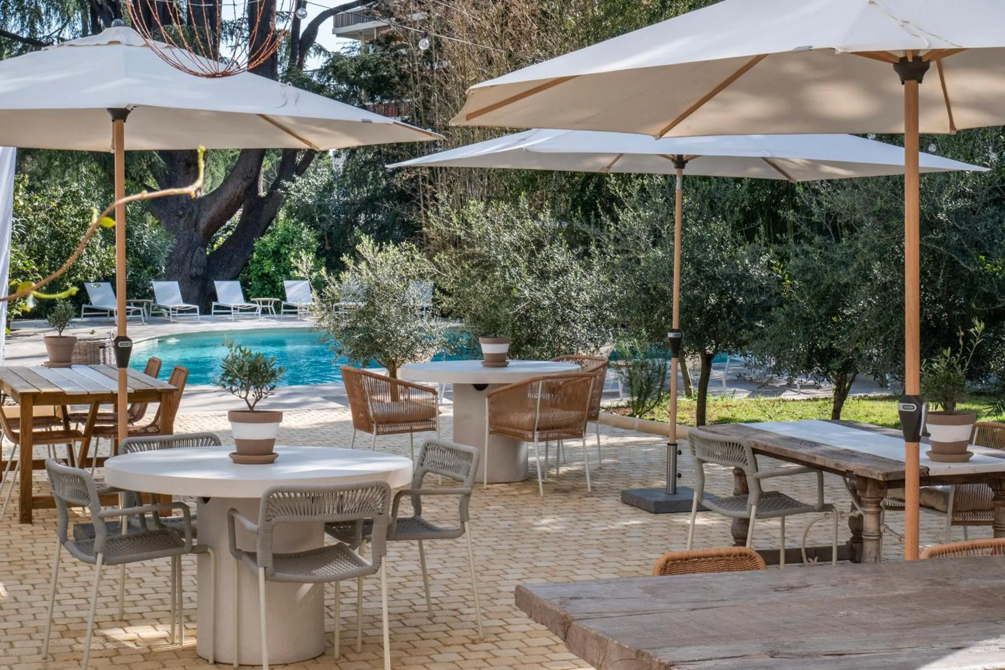 Tables et chaises disposées sur une terrasse pavée près d'une piscine.