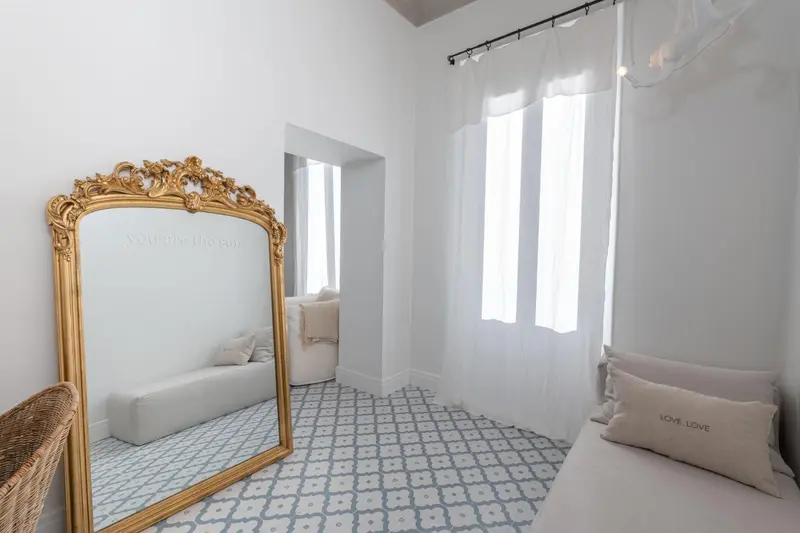 Une chambre lumineuse avec un grand miroir doré et un sol carrelé.