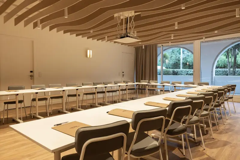 Une salle lumineuse est aménagée avec des tables et des chaises disposées en U.