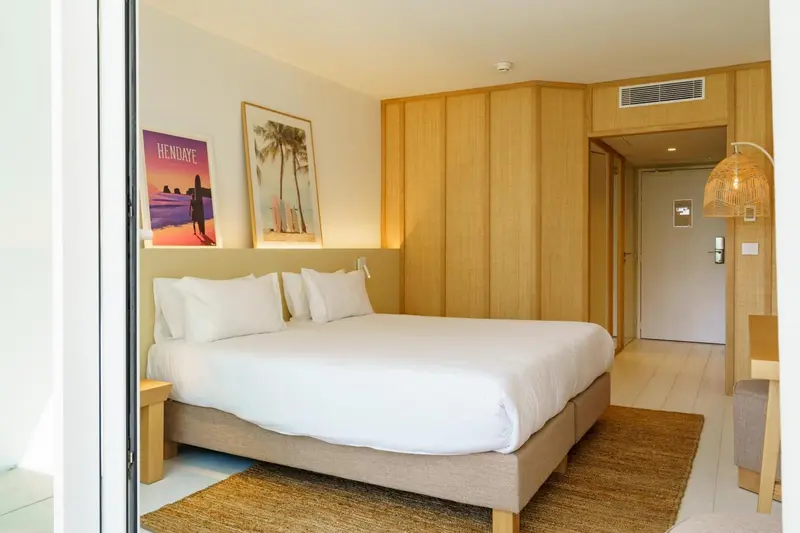 Une chambre lumineuse avec un grand lit recouvert de draps blancs et une décoration murale.