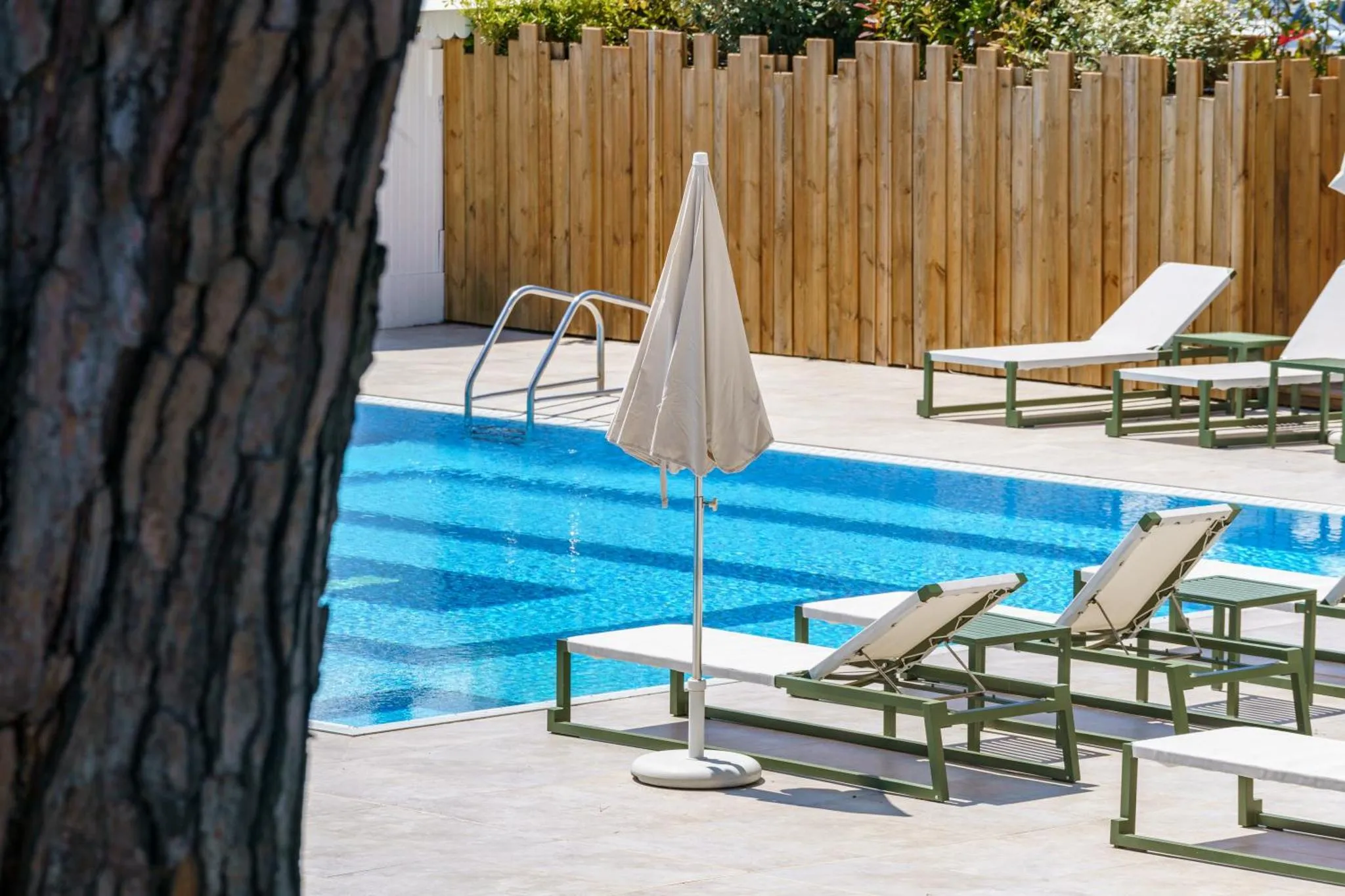 Transats blancs et parasol au bord d'une piscine bleue.