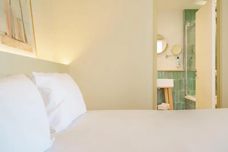 Lit préparé dans une chambre lumineuse avec salle de bain visible.