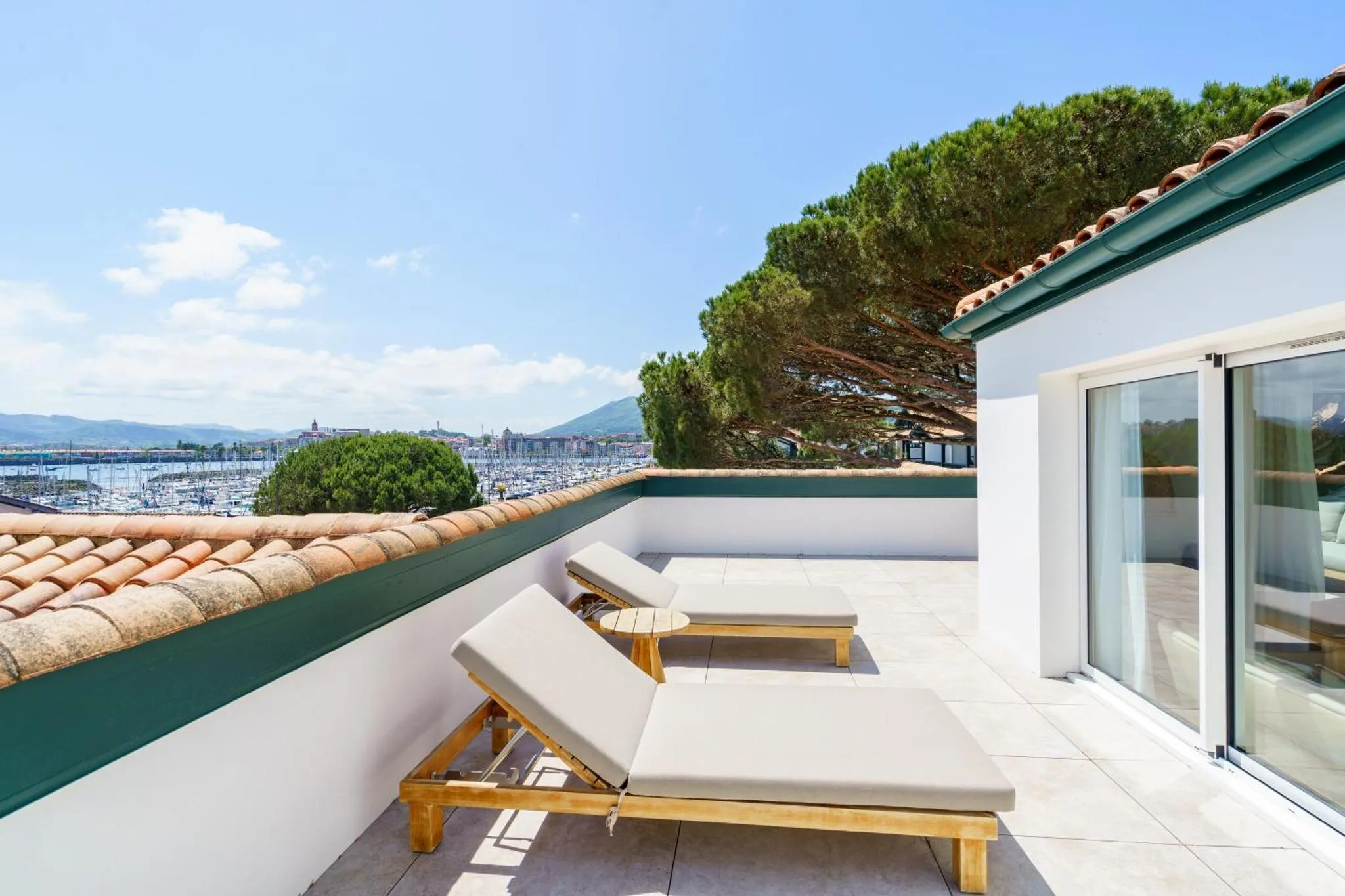 Deux transats sur une terrasse carrelée avec vue sur la mer et la ville.