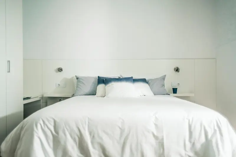 Un lit double recouvert de draps blancs et de coussins dans une chambre lumineuse.