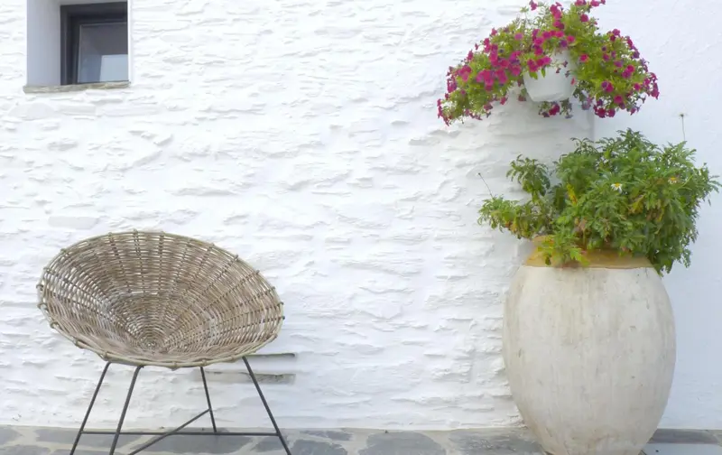 Une chaise en osier est placée devant un mur blanc orné de fleurs colorées.