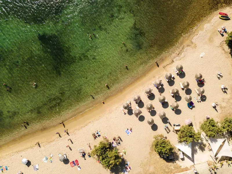 Vue aérienne d'une plage de sable fin bordée d'une eau turquoise et de parasols.