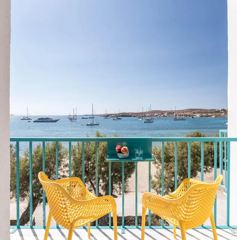 Deux fauteuils jaunes sur une terrasse avec vue sur la mer et des bateaux.
