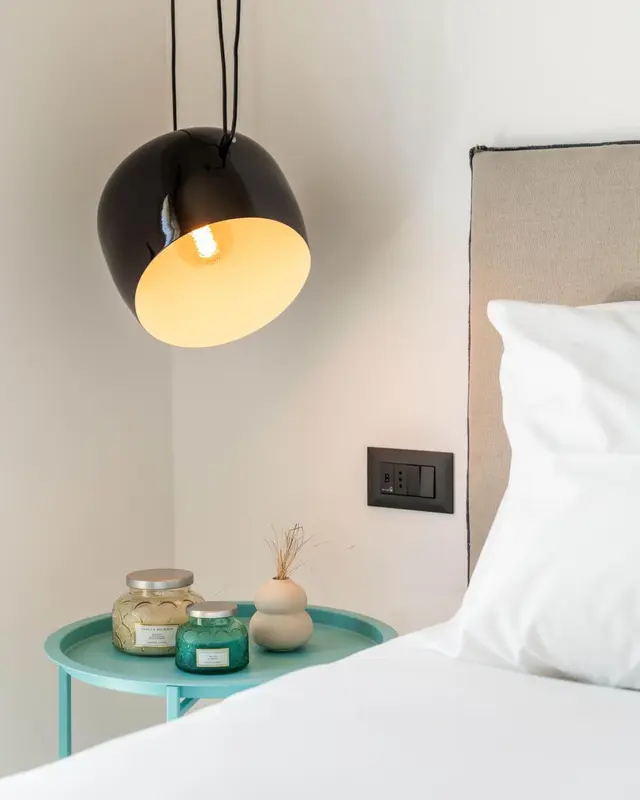 Une lampe suspendue éclaire une table de chevet turquoise avec des bougies et une petite plante.