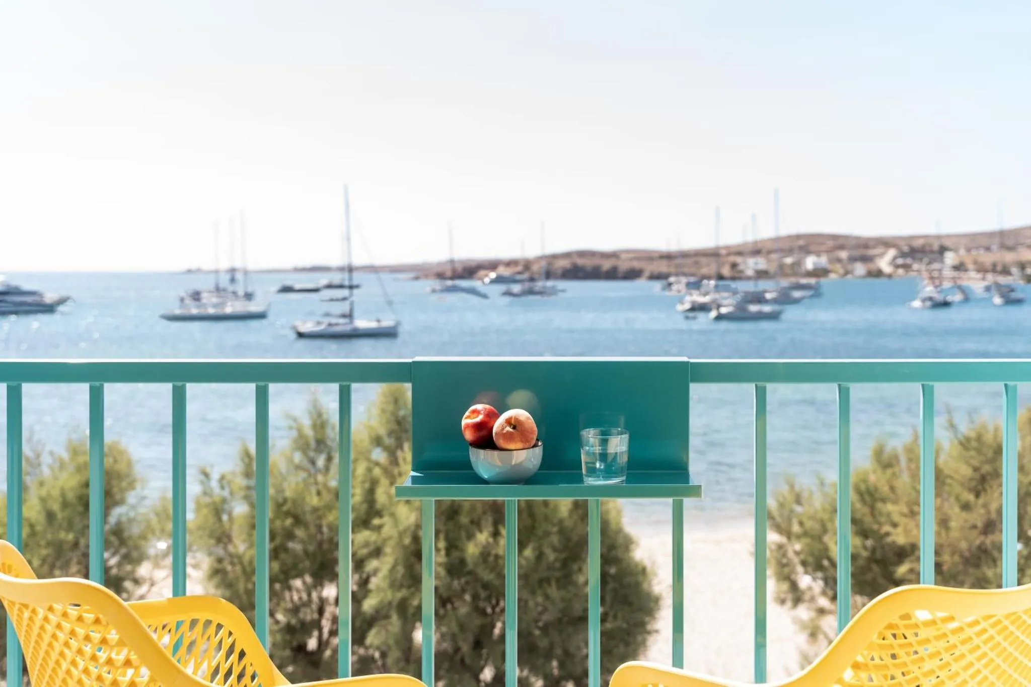 Une table avec des fruits et une boisson sur une terrasse donnant sur la mer et un port de plaisance.