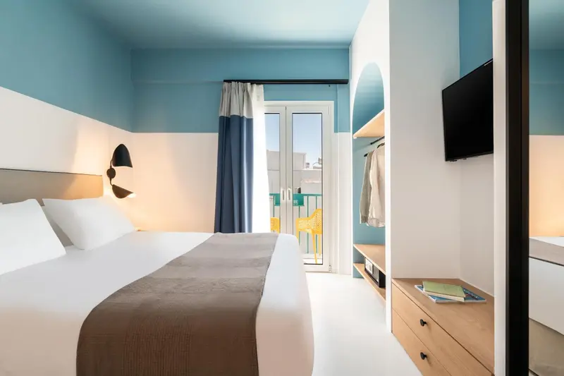 Une chambre lumineuse avec un lit fait et un accès à un balcon.