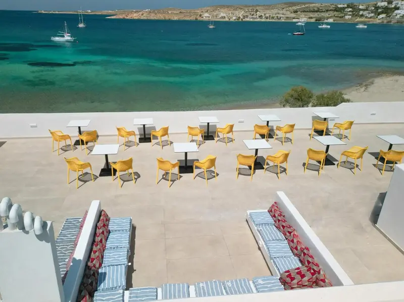 Terrasse aménagée avec tables et chaises, vue sur la mer turquoise et la côte.