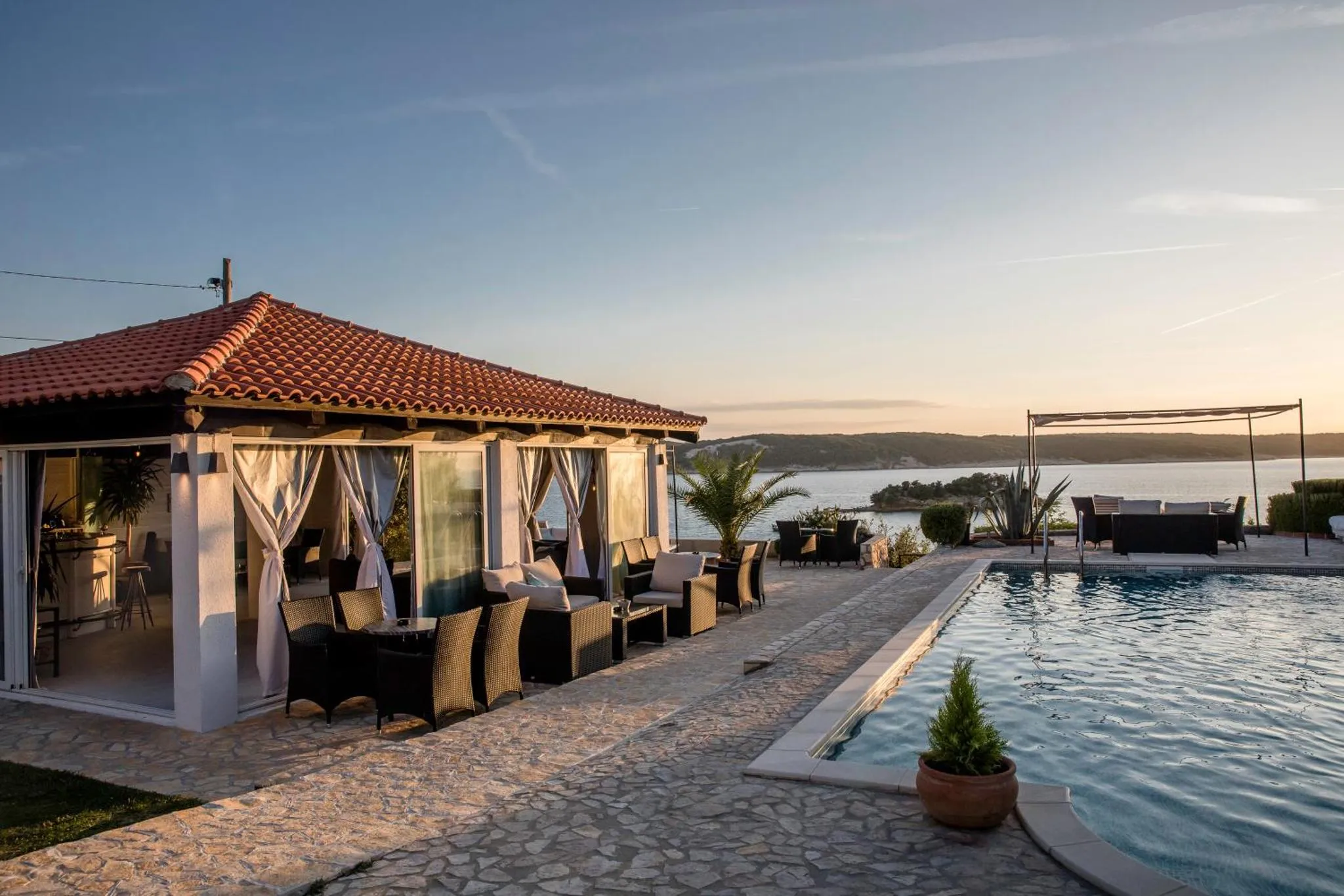 Terrasse ombragée avec mobilier de détente surplombant une piscine et la mer.