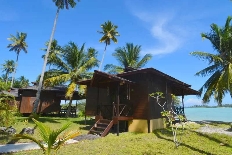Petites maisons en bois sur pilotis au milieu d'une végétation tropicale.