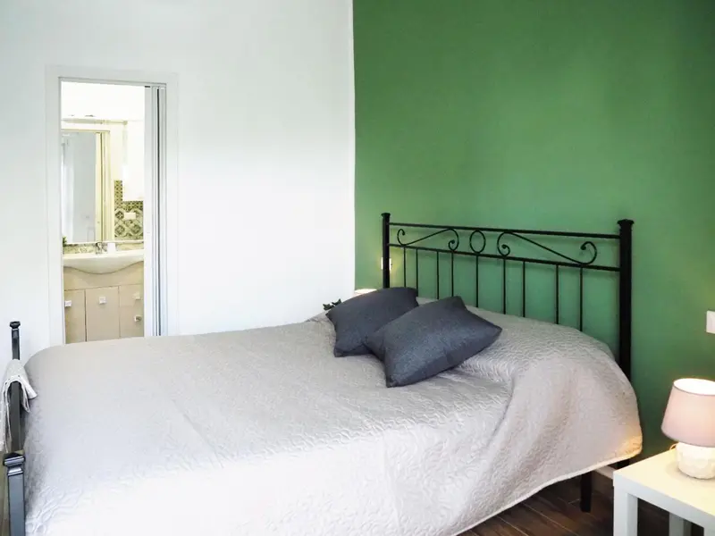 Une chambre lumineuse avec un lit recouvert d'une courtepointe et un mur vert.