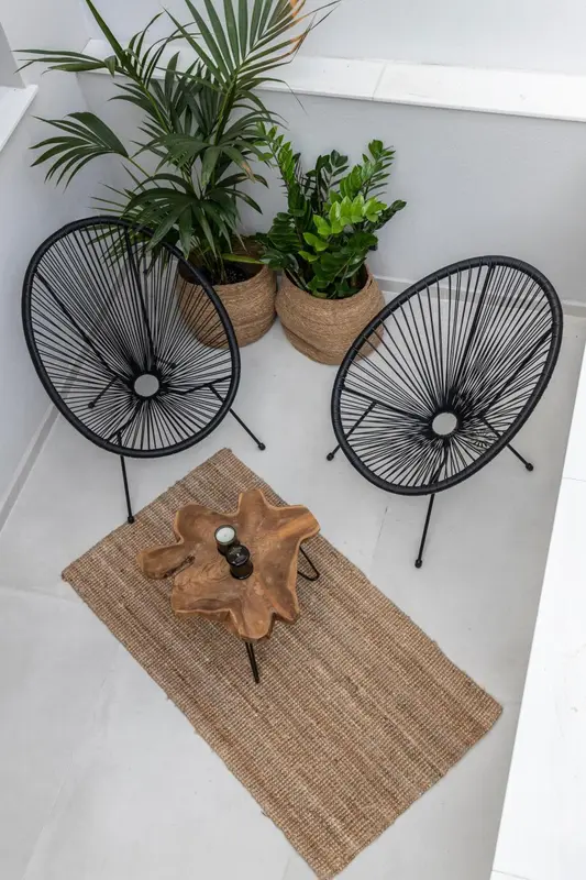 Deux fauteuils en osier noir sont disposés sur un tapis en fibres naturelles près d'une table basse en bois.
