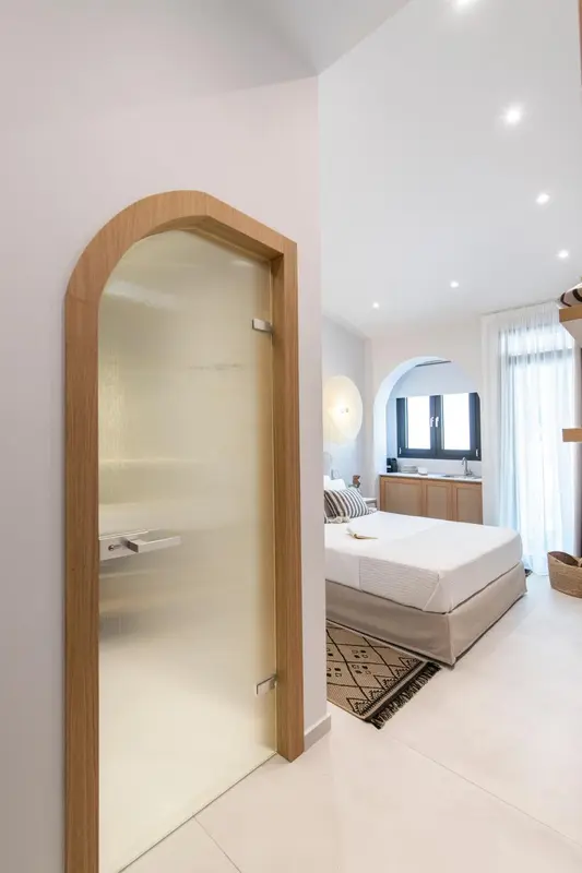 Une chambre lumineuse avec un lit fait et une salle de bain visible à travers une ouverture en arc.