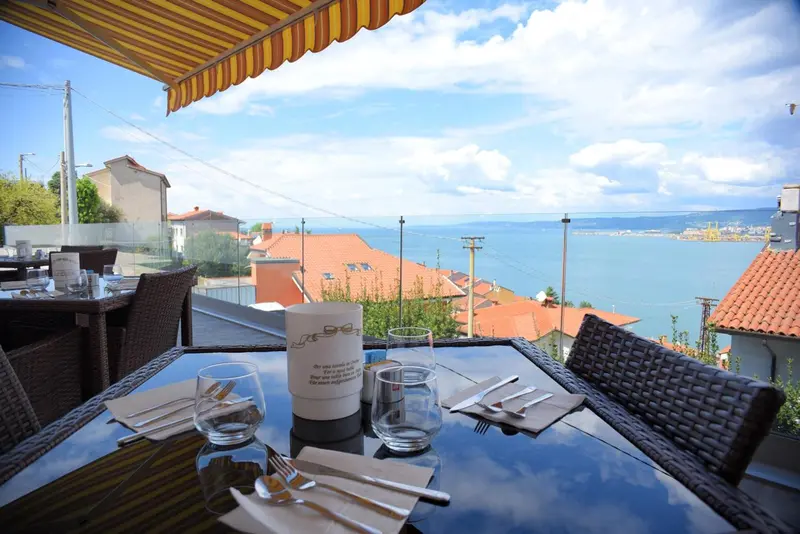 Une table est dressée sur une terrasse avec vue sur la mer et les toits.
