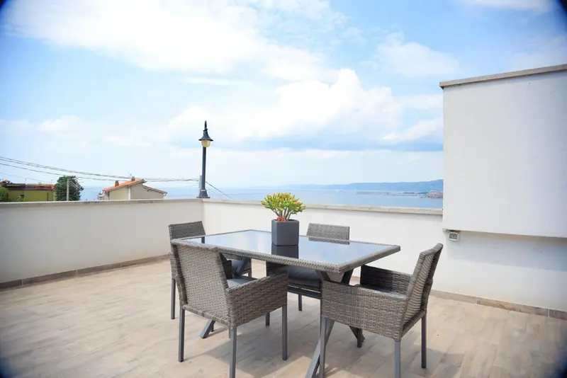 Une table et des chaises en osier composent un espace repas sur une terrasse ensoleillée.
