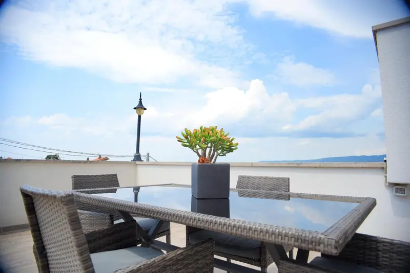 Table et chaises sur une terrasse ensoleillée avec vue sur la mer.