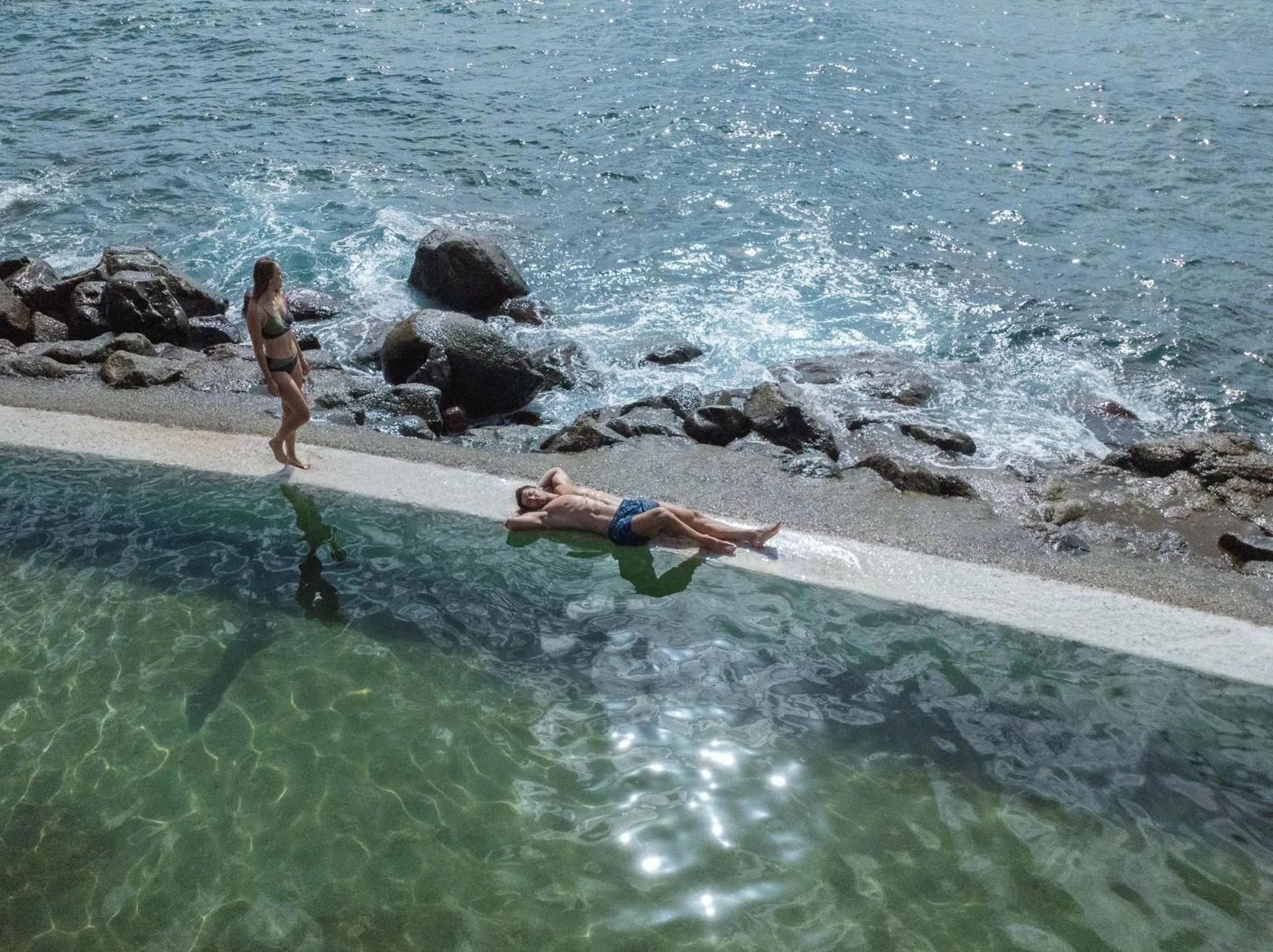 Deux personnes se détendent au bord d'une piscine naturelle rocheuse.