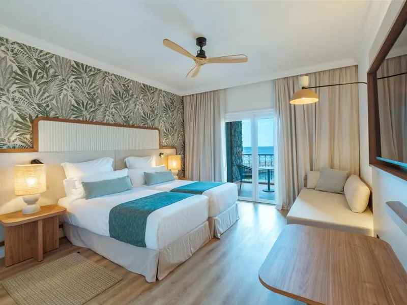 Chambre lumineuse avec deux lits simples et vue sur la mer.
