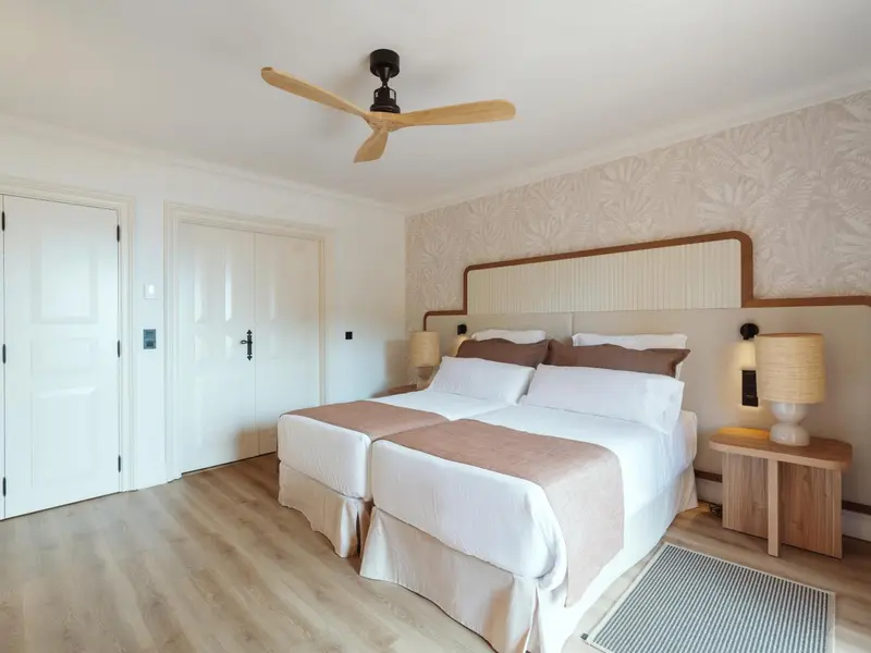 Une chambre lumineuse avec deux lits simples et un ventilateur de plafond.