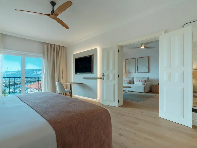 Une chambre lumineuse avec un grand lit et un espace salon attenant.