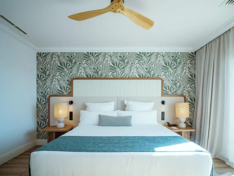 Une chambre lumineuse avec un grand lit et un mur décoré de motifs végétaux.