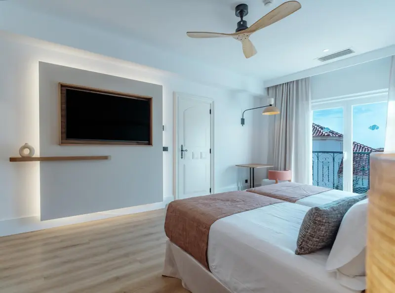 Chambre lumineuse avec un grand lit et une télévision murale.