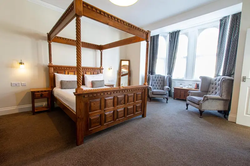 Une chambre spacieuse avec un lit à baldaquin et deux fauteuils.