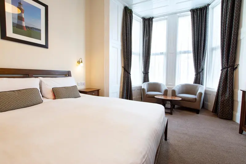 Une chambre lumineuse avec un grand lit et deux fauteuils près d'une fenêtre.