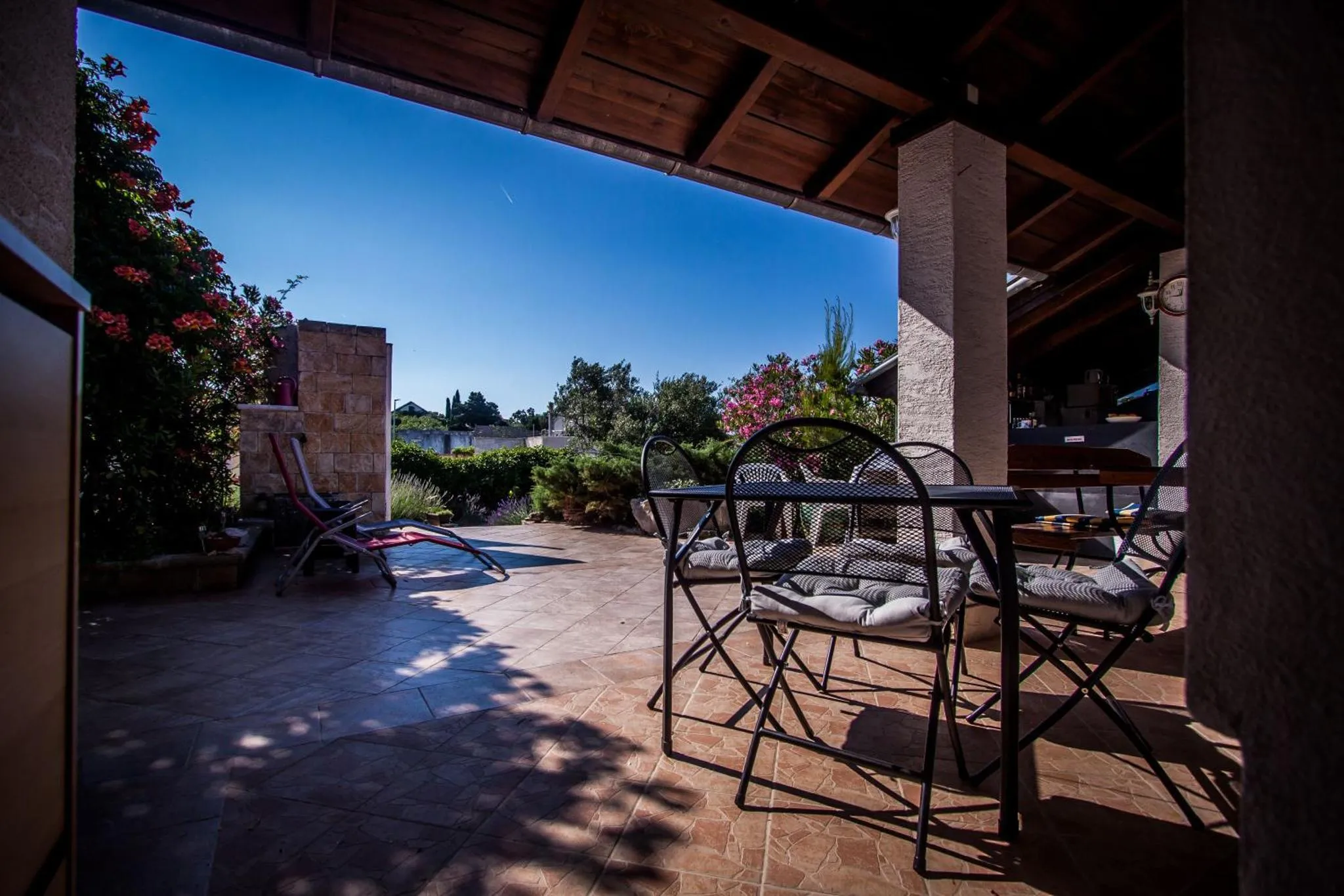 Terrasse ombragée avec table et chaises donnant sur un jardin fleuri.
