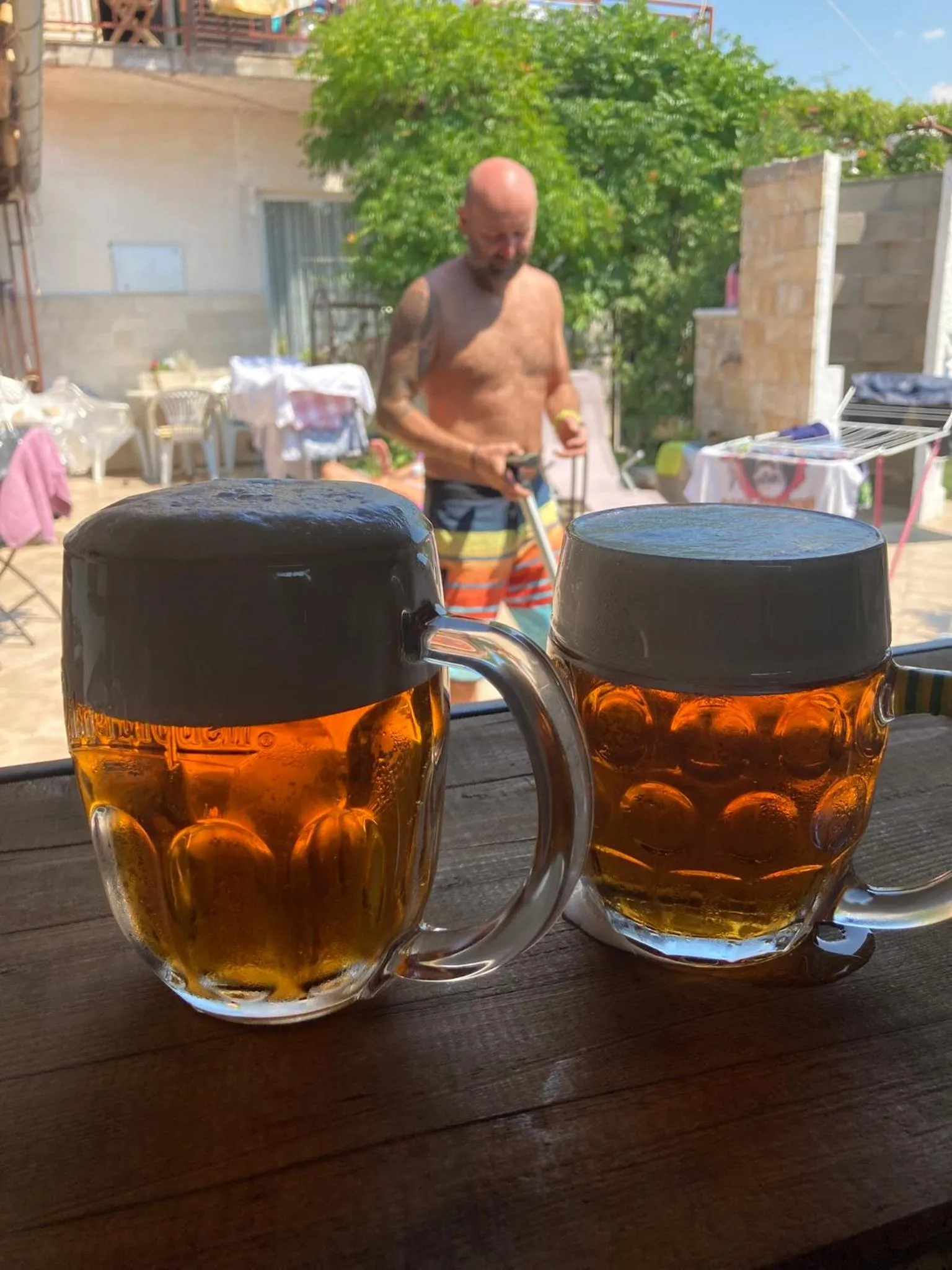 Deux grands verres de bière sur une table en bois, avec une personne floue en arrière-plan.