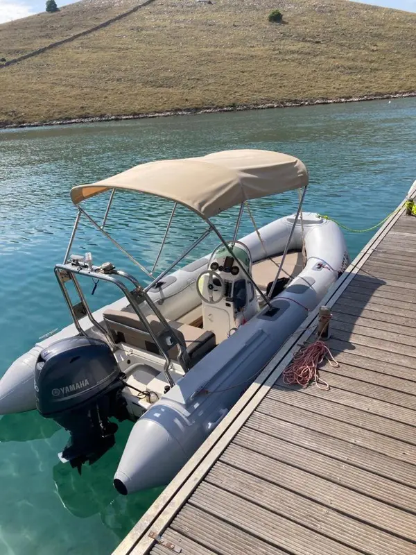 Un bateau pneumatique amarré à un ponton en bois sur une eau turquoise.