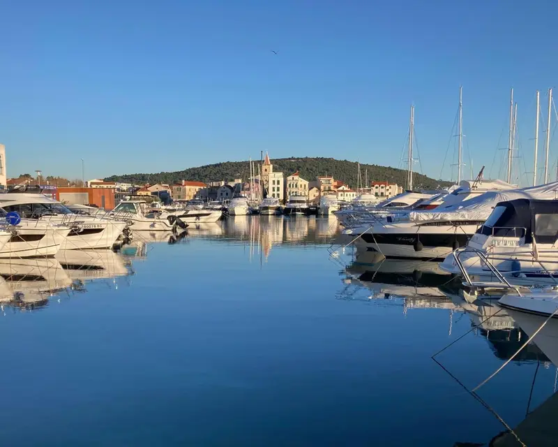 Port de plaisance ensoleillé avec des bateaux à quai et une ville en arrière-plan.